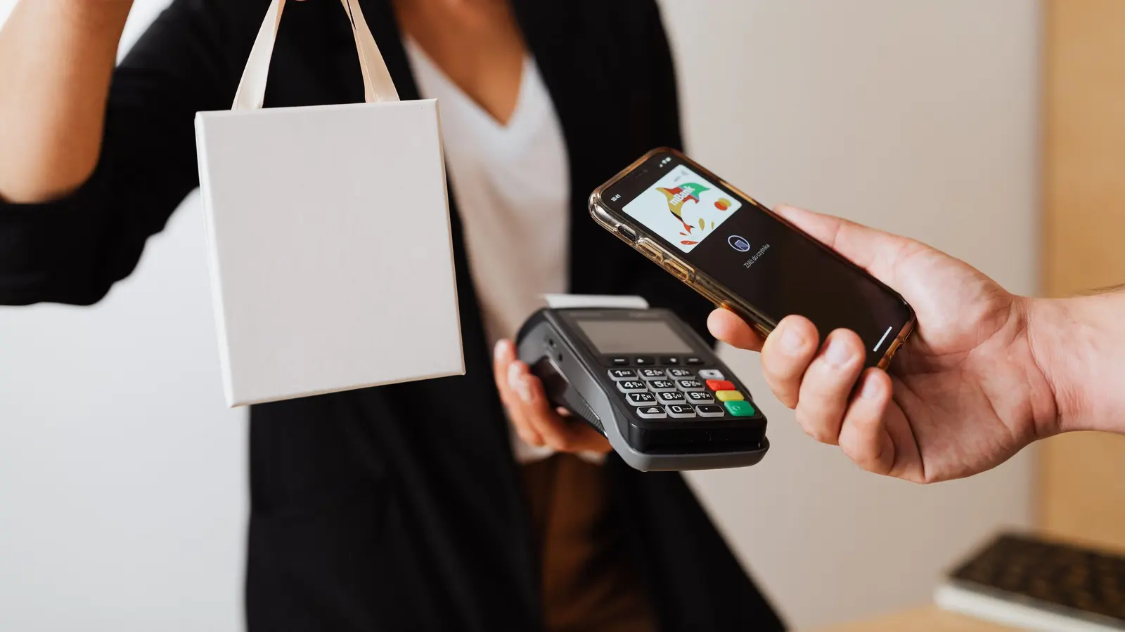 Un client approche son téléphone d'un terminal de paiement, sac de courses à la main