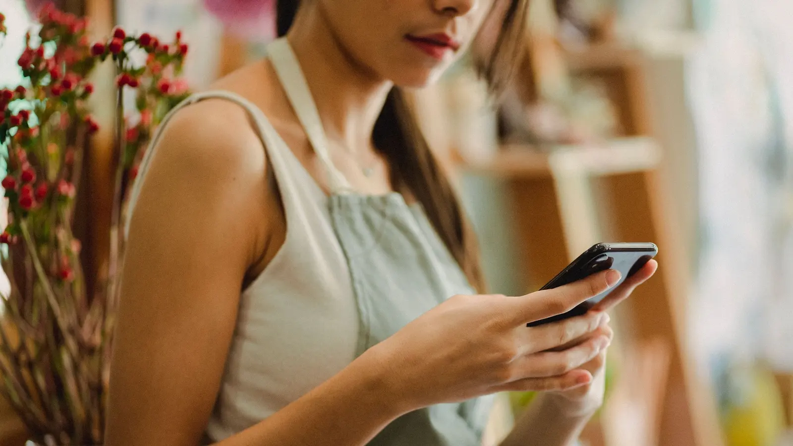 Une fleuriste en tablier consulte son téléphone dans sa boutique